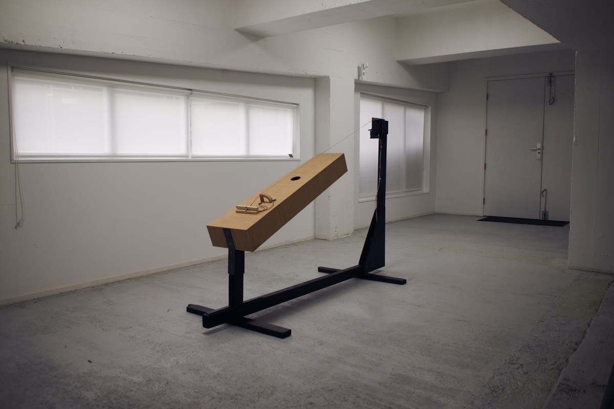 Photograph of the trombone marino from the side: the wooden body tilted up on the welded steel frame, the motor head at the top of the upright
